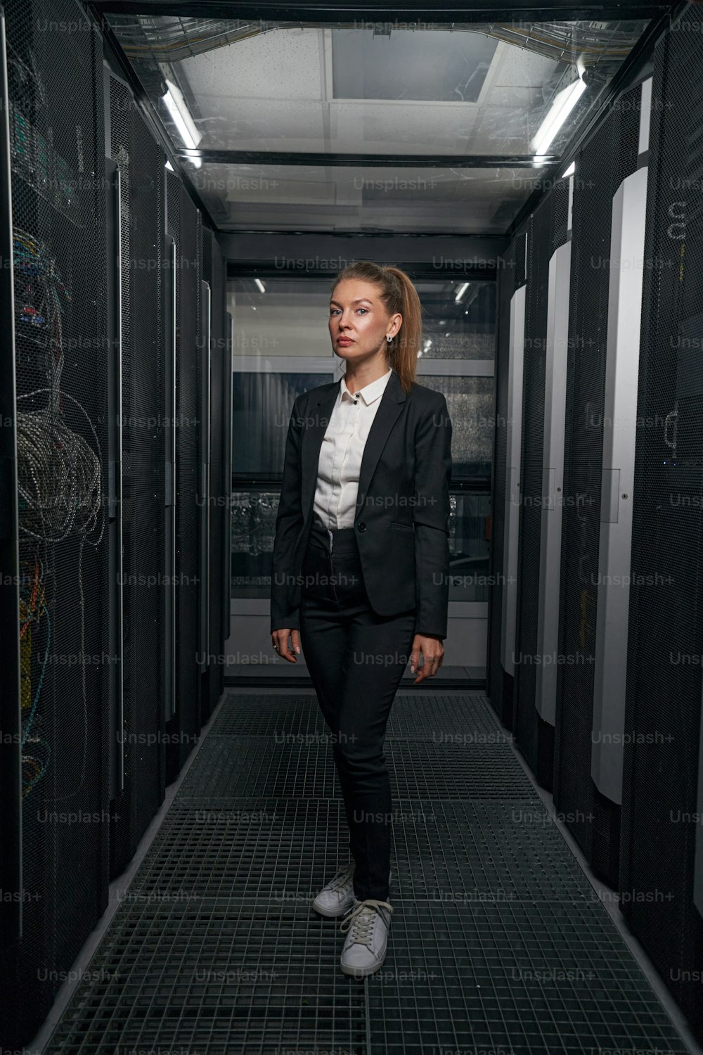 Jeune femme manager sérieuse debout dans la salle des serveurs d’un centre de données moderne