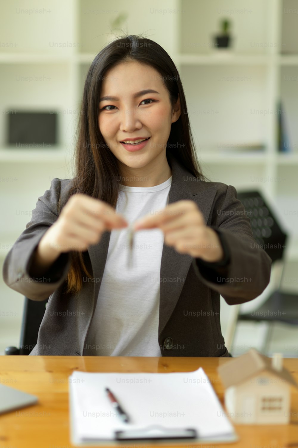 Portrait of Beautiful young asian house Real Estate Agent broker sits at her desk and hold house keychain.