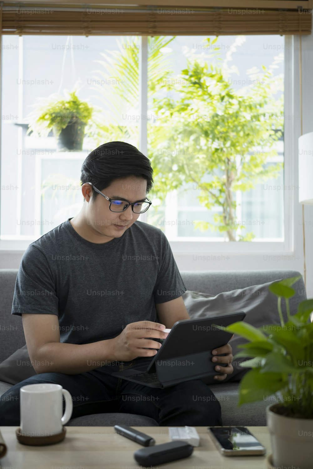 Young asian man working online with computer tablet while sitting on couch.