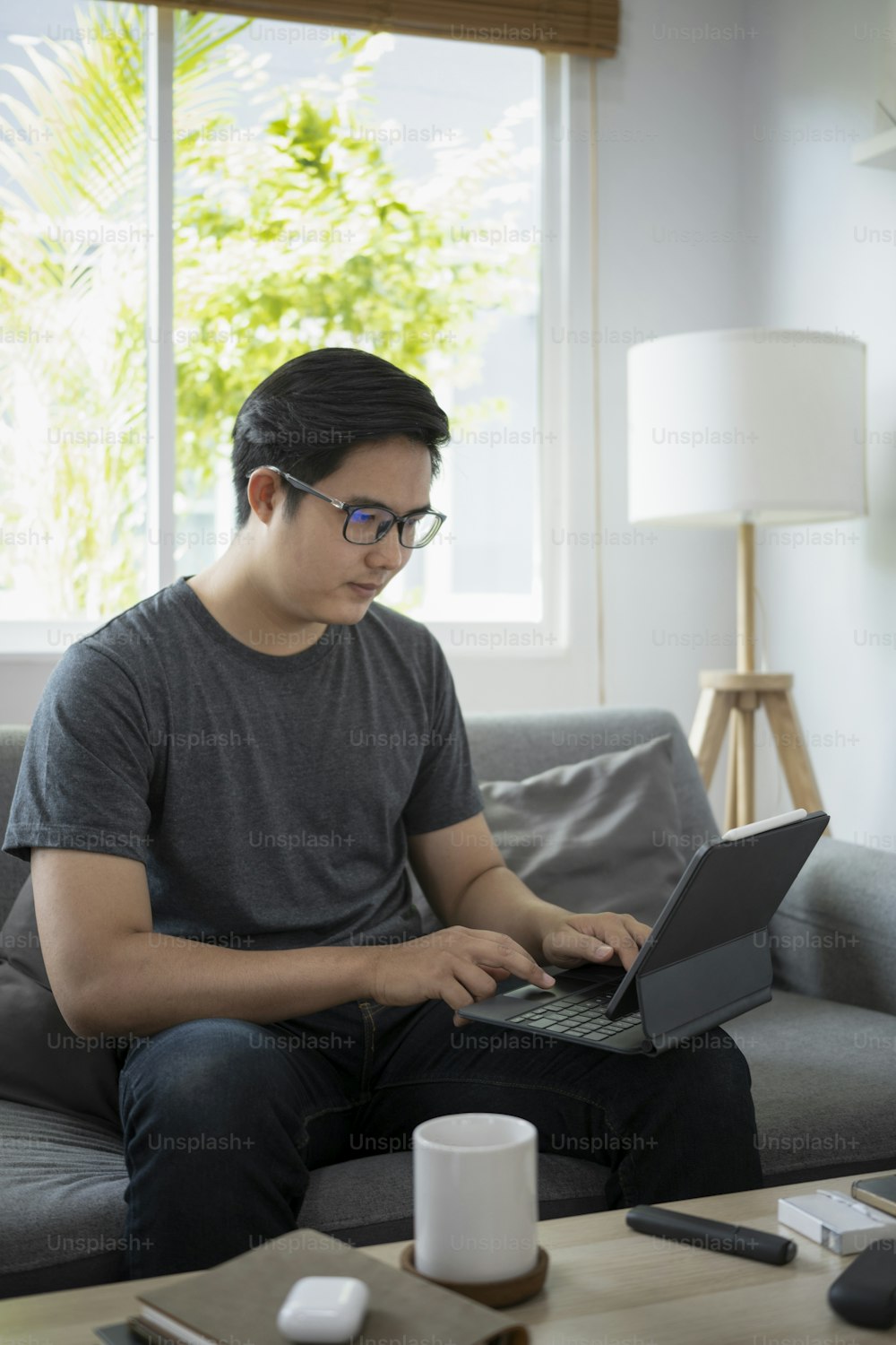Handsome asian man sitting on sofa and working online with computer tablet.