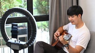 若いアジアの男性のビデオブロガーは、ギターを弾き、彼のブログのビデオコンテンツを記録しています。