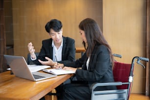 Businesswoman in wheelchair working on new business project with her colleague in office.