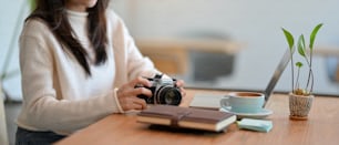 Cropped image of Female freelancer photo grapher with retro vintage camera, laptop and her stuff on table at coffee shop