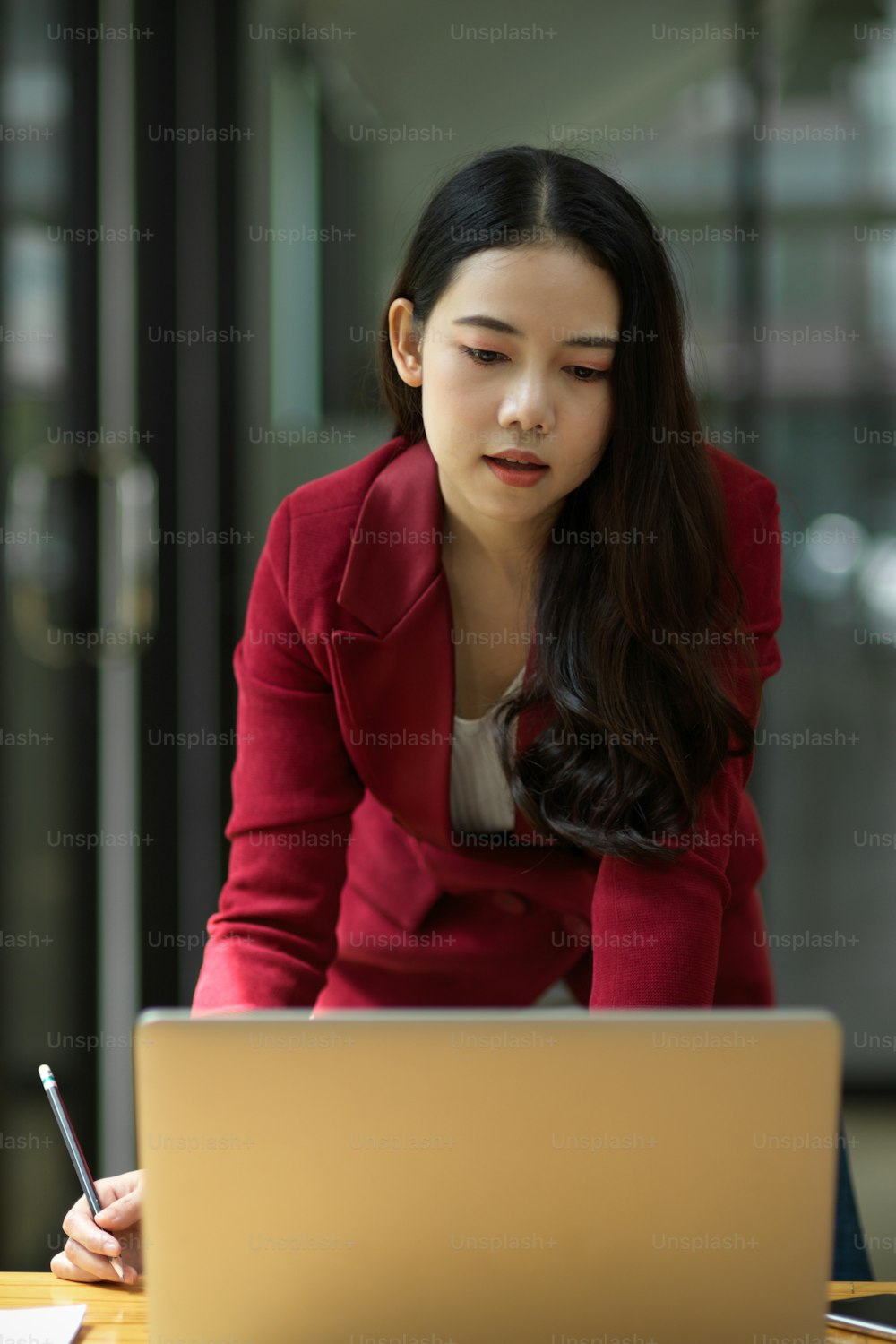 Porträt einer selbstbewussten und smarten jungen asiatischen Geschäftsfrau, die im Büro an ihrem Laptop arbeitet