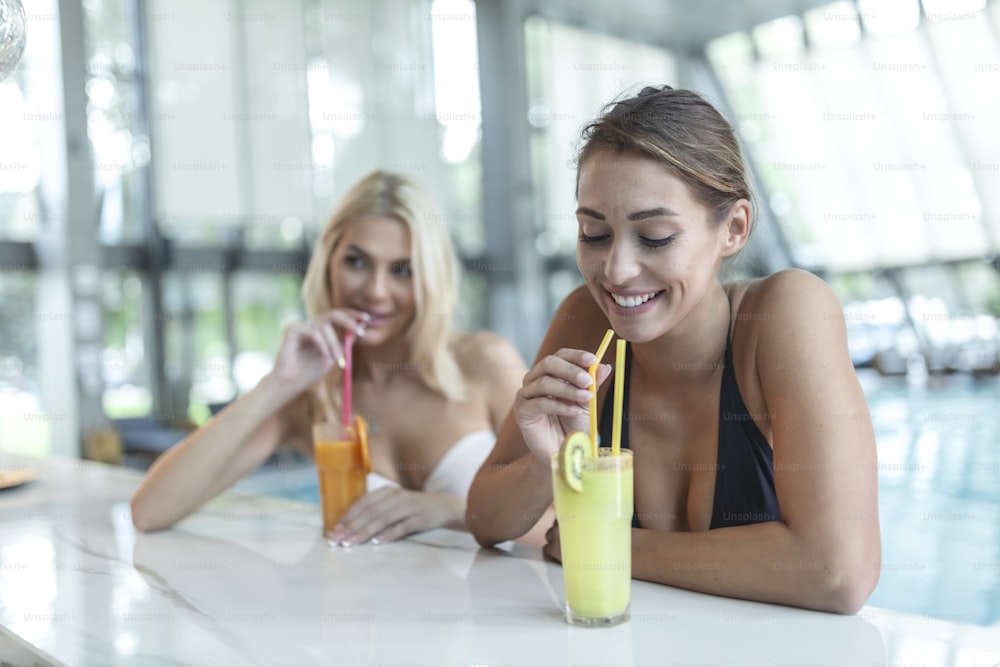 Dos hermosas mujeres relajándose en la piscina con cocktails.pool bar en el destino de vacaciones del complejo turístico tropical
