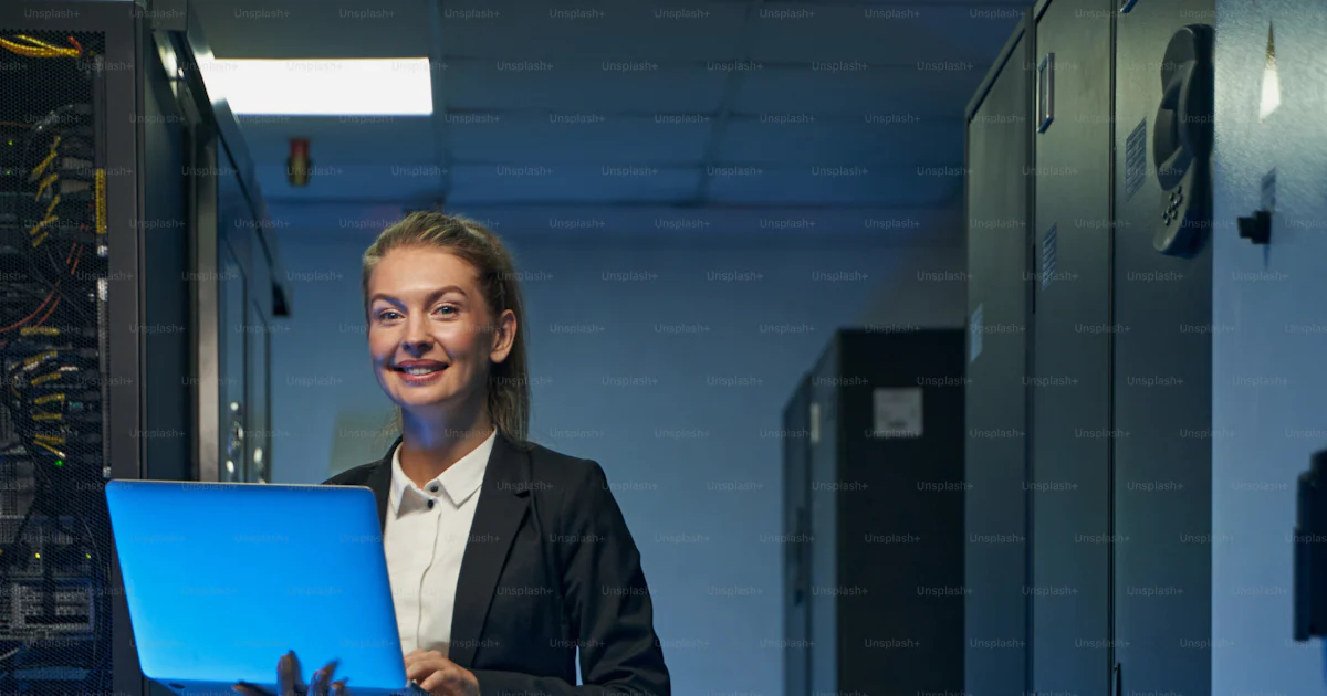 Happy female administrator in elegant suit working with laptop computer ...