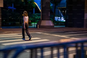 Retrato de una joven hermosa mujer asiática que camina en el paso de peatones de la calle en la ciudad y mira a la multitud de personas y las luces nocturnas iluminadas. La chica bonita disfruta del estilo de vida urbano al aire libre y la vida nocturna de la ciudad.