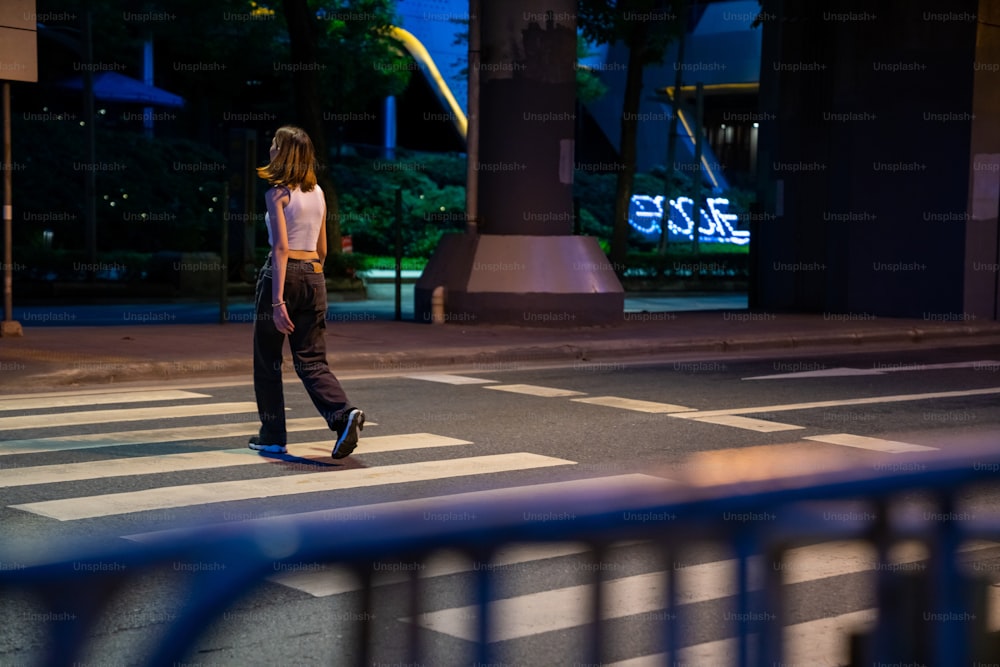 Retrato de una joven hermosa mujer asiática que camina en el paso de peatones de la calle en la ciudad y mira a la multitud de personas y las luces nocturnas iluminadas. La chica bonita disfruta del estilo de vida urbano al aire libre y la vida nocturna de la ciudad.