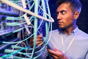 Serious focused data center system administrator monitoring fiber optic cables in server room