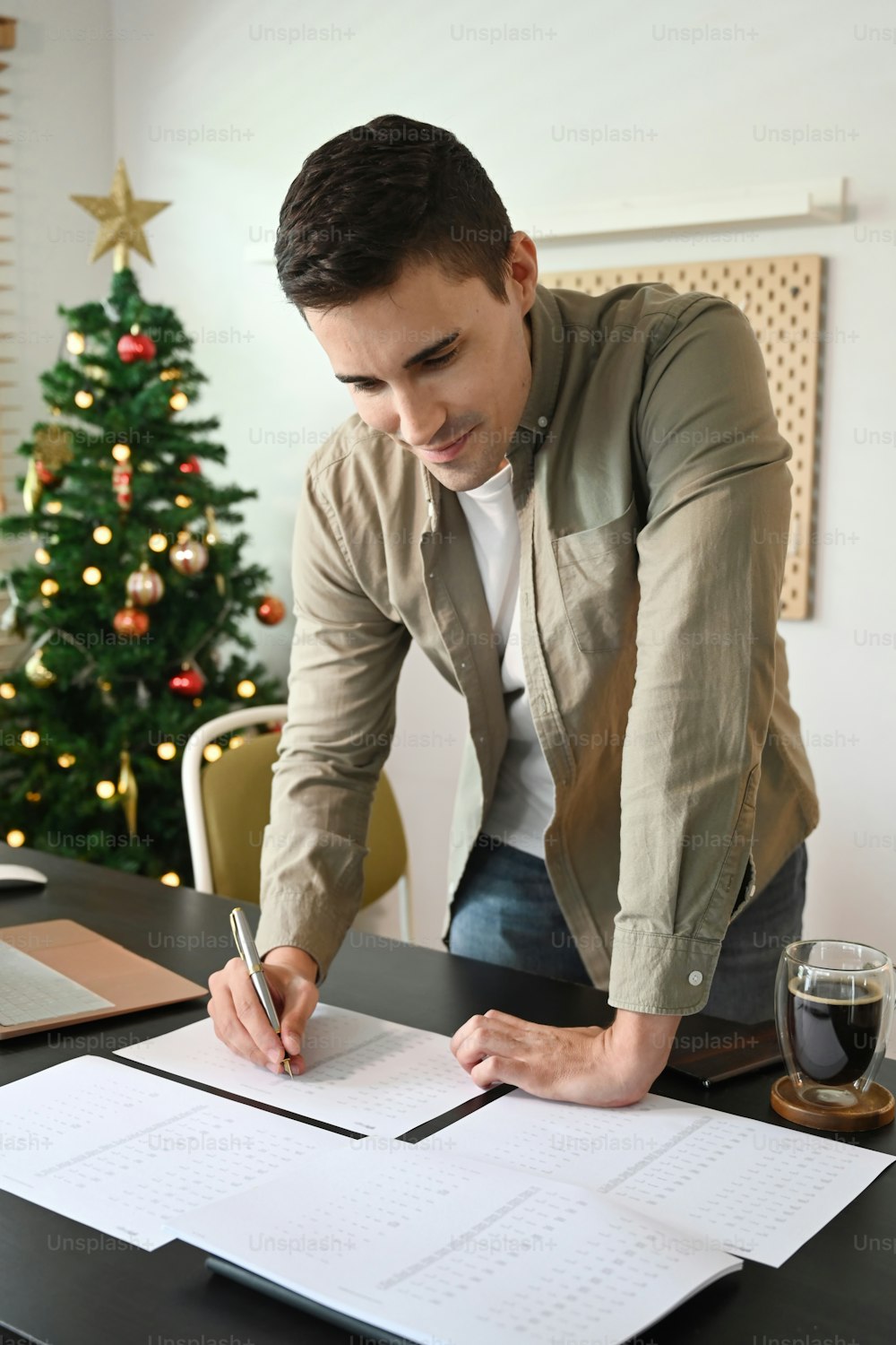 Smiling man standing in home office and checking reports on wooden table.