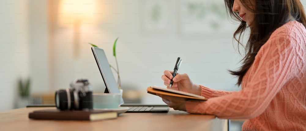 Vista lateral da bela mulher de negócios em suéter rosa senta-se em um café elegante escrever algo, plano de negócios, ideia criativa em seu caderno.