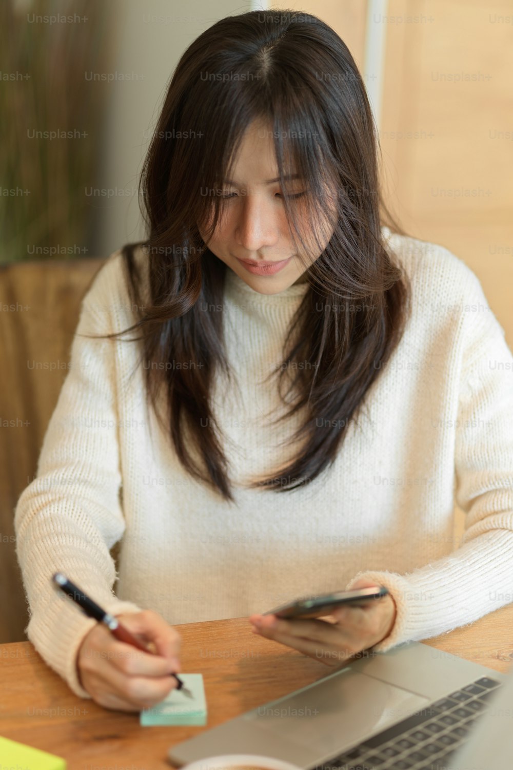 Portrait of young asian female taking notes on memo pads while looking on mobile screen, working from home.