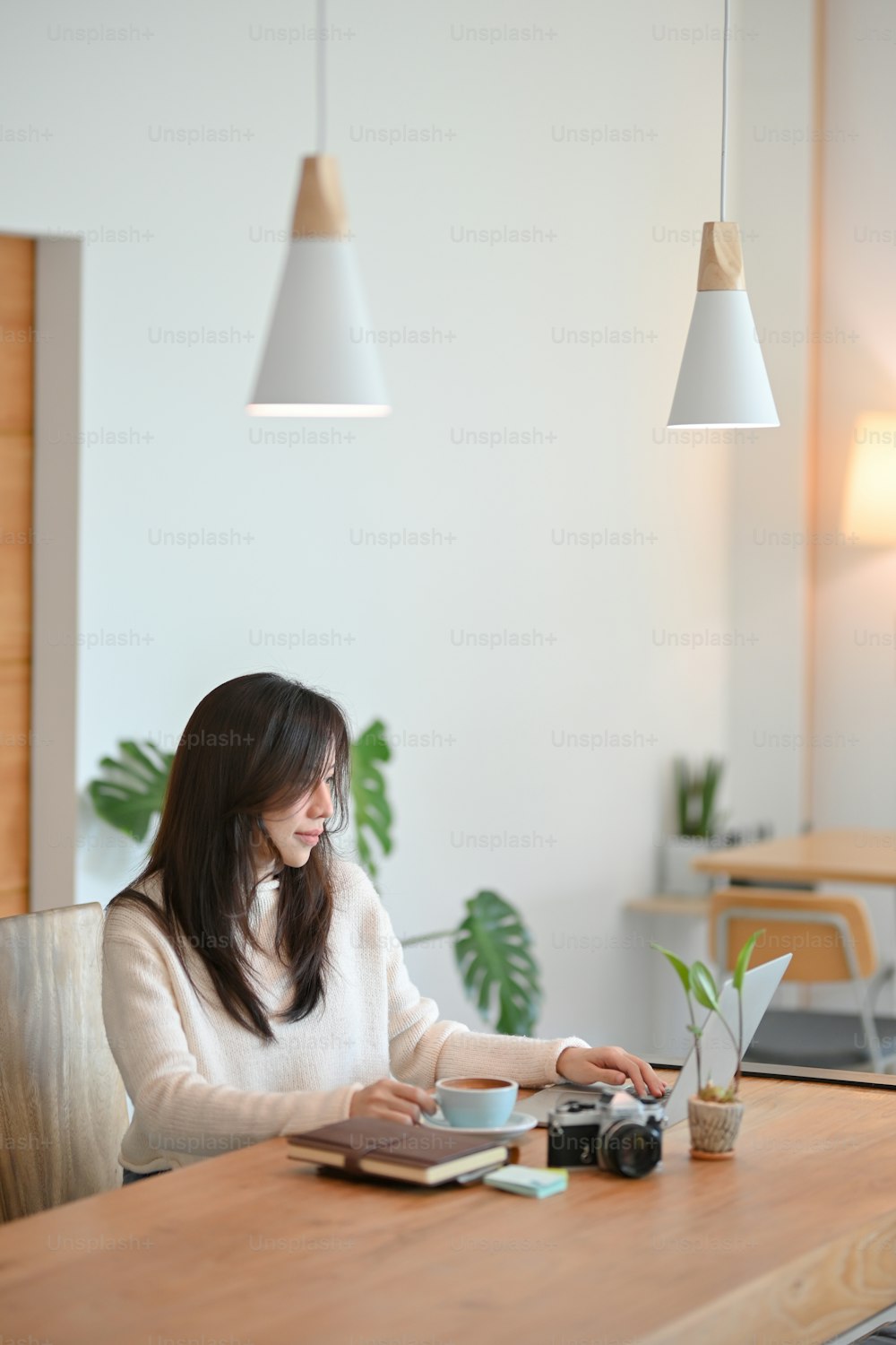 Charmante junge asiatische Café- oder Reisebloggerin, die an ihrem Laptop in einem modernen, stilvollen Café arbeitet