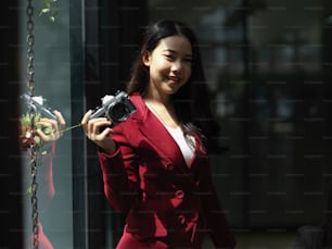 Giovane femmina asiatica in abito rosso con foto retrò o macchina fotografica vintage in piedi nel moderno ufficio dello studio