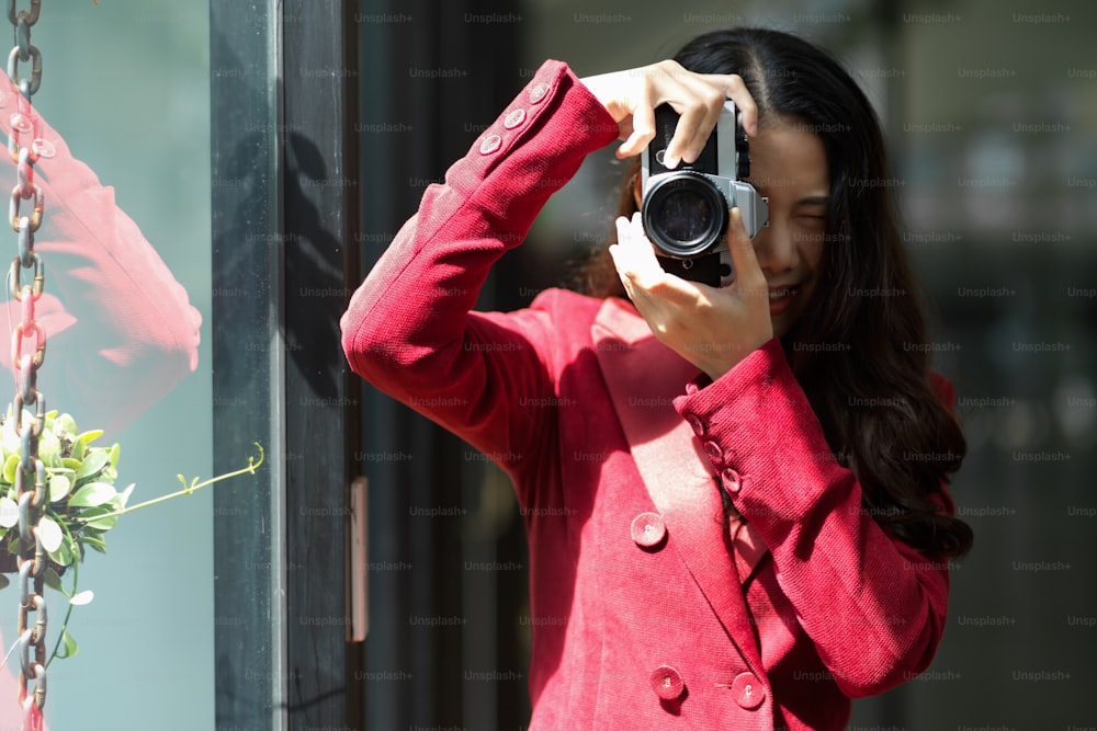 Millennial female in elegant red suit using vintage retro camera in studio, snapshot, portrait, photographer, hobby.