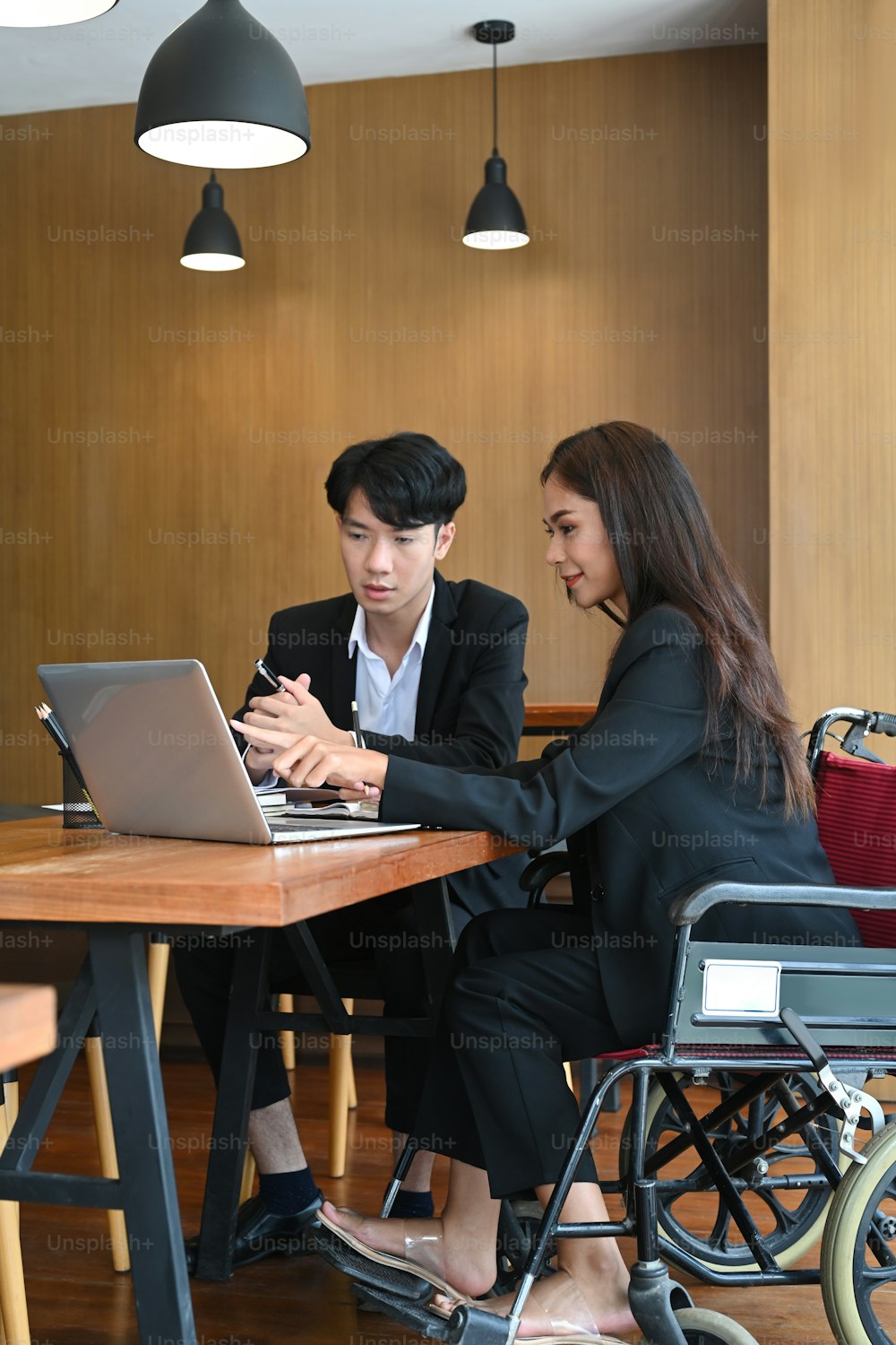 Smiling businesswoman in a wheelchair working in office with her colleague.