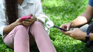 Giovane donna ritagliata che si siede nel parco con il suo ragazzo e usa lo smartphone.