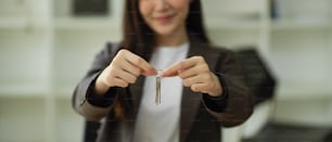 Cropped image of female real estate agent showing house keys chain to camera. Property business concept