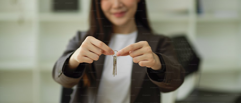 Beschnittenes Bild einer Immobilienmaklerin, die Hausschlüsselanhänger zur Kamera zeigt. Immobilien-Geschäftskonzept