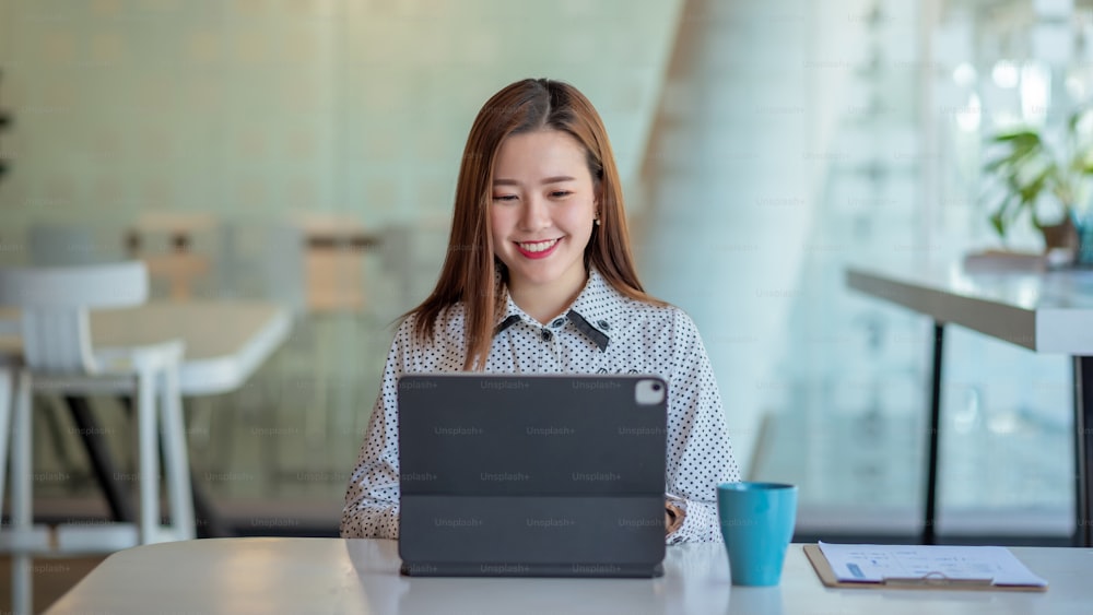 Jeune femme d’affaires asiatique belle charmante souriante et utilisant une tablette numérique au bureau.