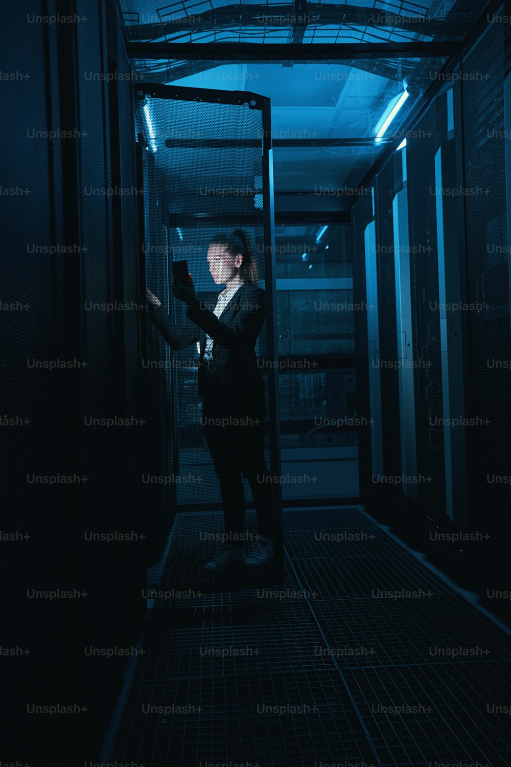 데이터 센터의 어두운 방에서 서버 랙에서 하드웨어를 확인하는 휴대폰을 가진 여성 IT 관리자