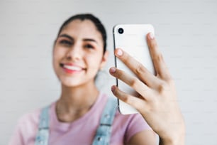 Joven mujer latina toma selfie de las manos del teléfono sobre fondo gris en América Latina