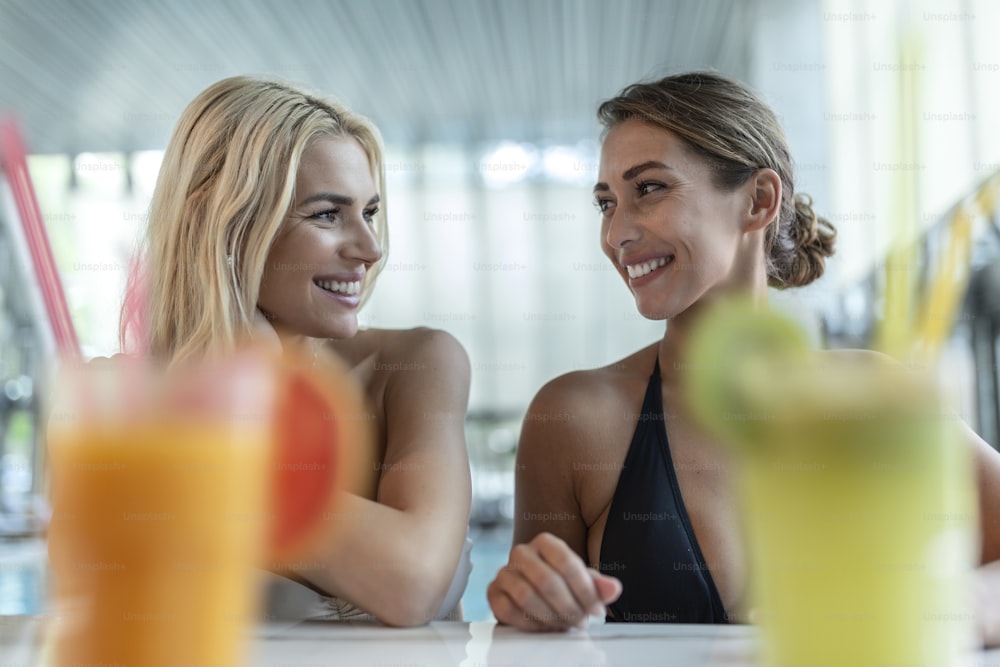 Young women drinking cocktail in swimming pool bar. Idyllic summer vacation concept.