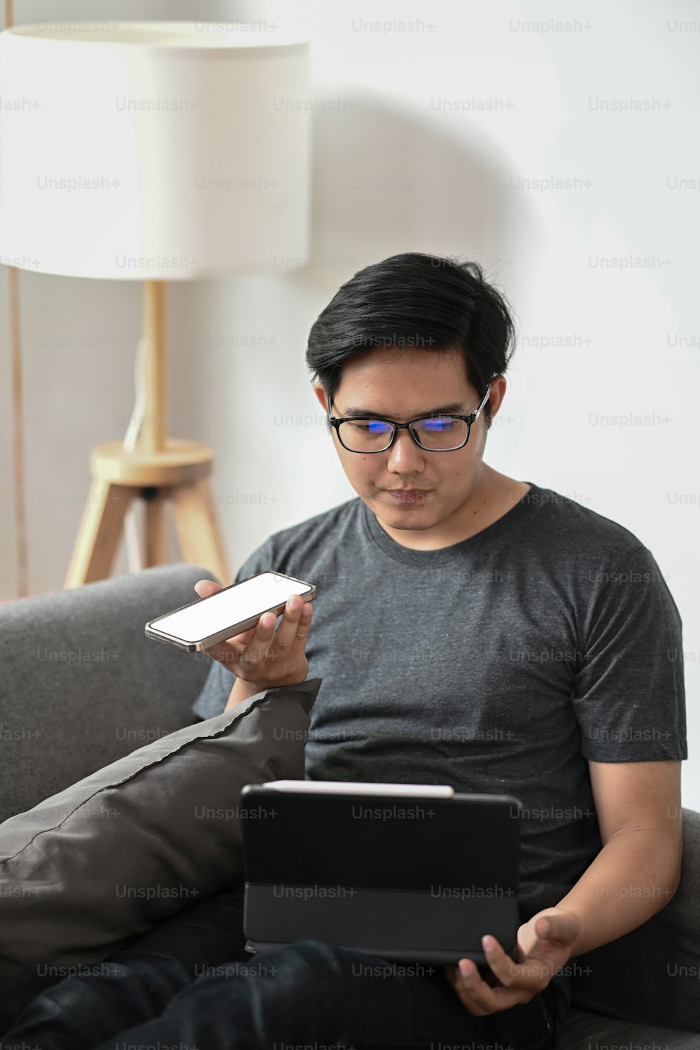 Man talking on smart phone and working with computer tablet in living room.