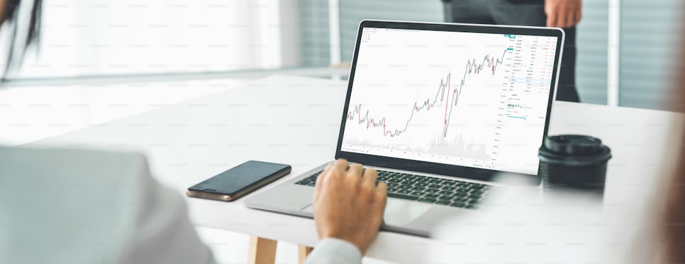 Businesswoman in analyze stock market data using laptop computer proficiently at the office while attending a group meeting with business team .