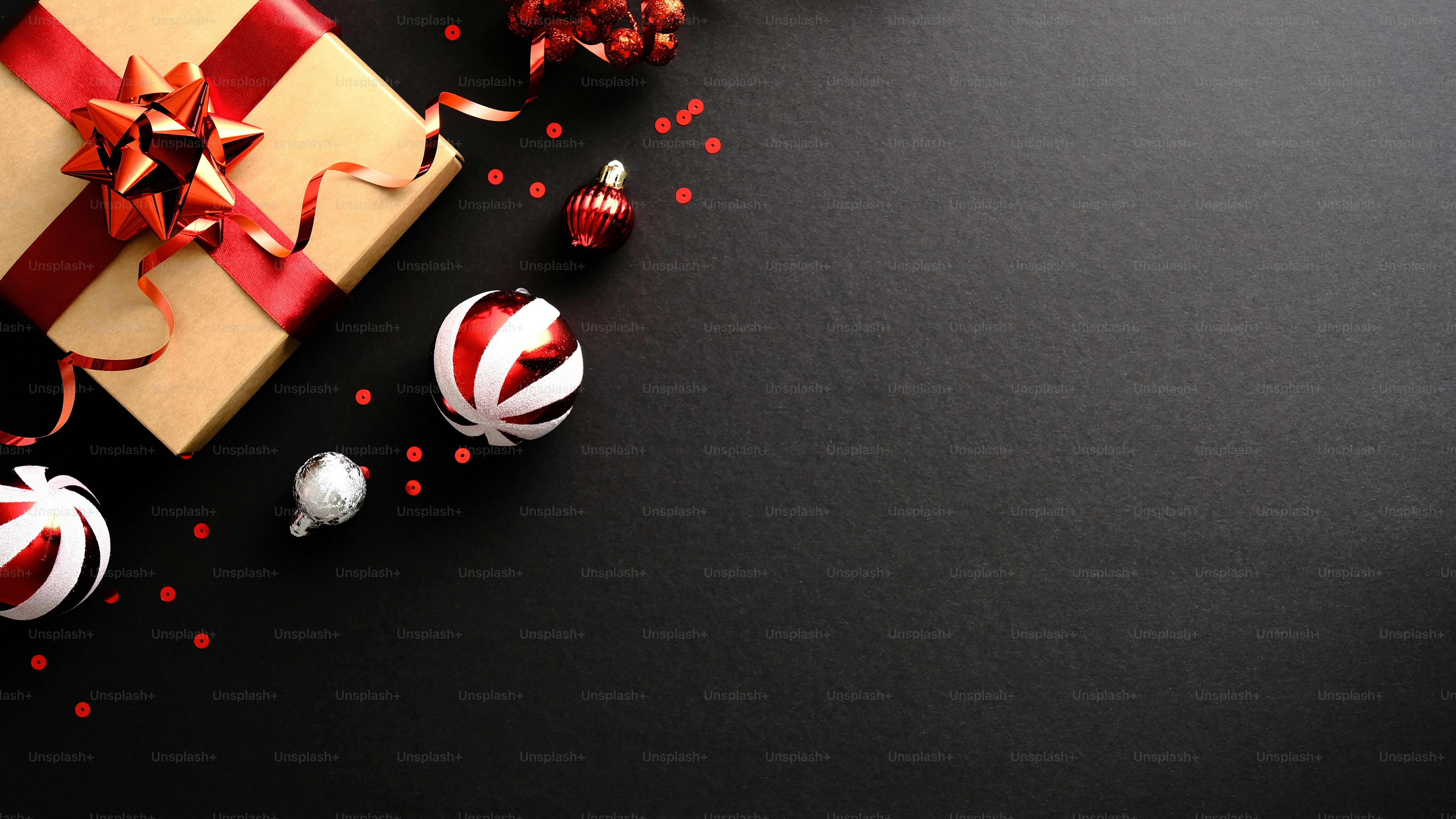 Luxury Christmas banner design. Christmas gift box wrapped red ribbon, striped bauble, confetti, decorations on dark black background. Black Friday, Christmas sale concept. Copy space. Top view.