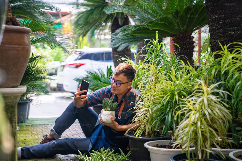 Propietario de una tienda de plantas de jardinero asiático moderno en vivo en plantas en macetas de presentación de teléfonos inteligentes para compras en línea en las redes sociales. Empresario de pequeñas empresas que trabaja con el concepto de tecnología