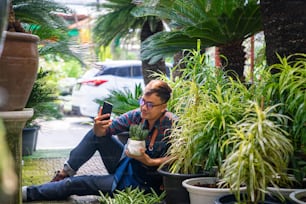 Modern Asian man gardener plant shop owner live streaming on smartphone presentation potted plants for online shopping on social media. Small business entrepreneur working with technology concept