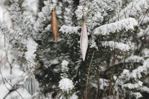 Moderner Weihnachtsschmuck hängt an verschneitem Kiefernzweig. Geschmückter Weihnachtsbaum mit stilvollen Kugeln im Schnee im Freien. Winterurlaub auf dem Land. Frohe Weihnachten! Platz für Text