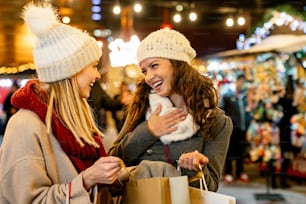 Vendita di Natale e concetto di persone. Giovani amiche felici con borse della spesa che si godono lo shopping nel mercatino di natale