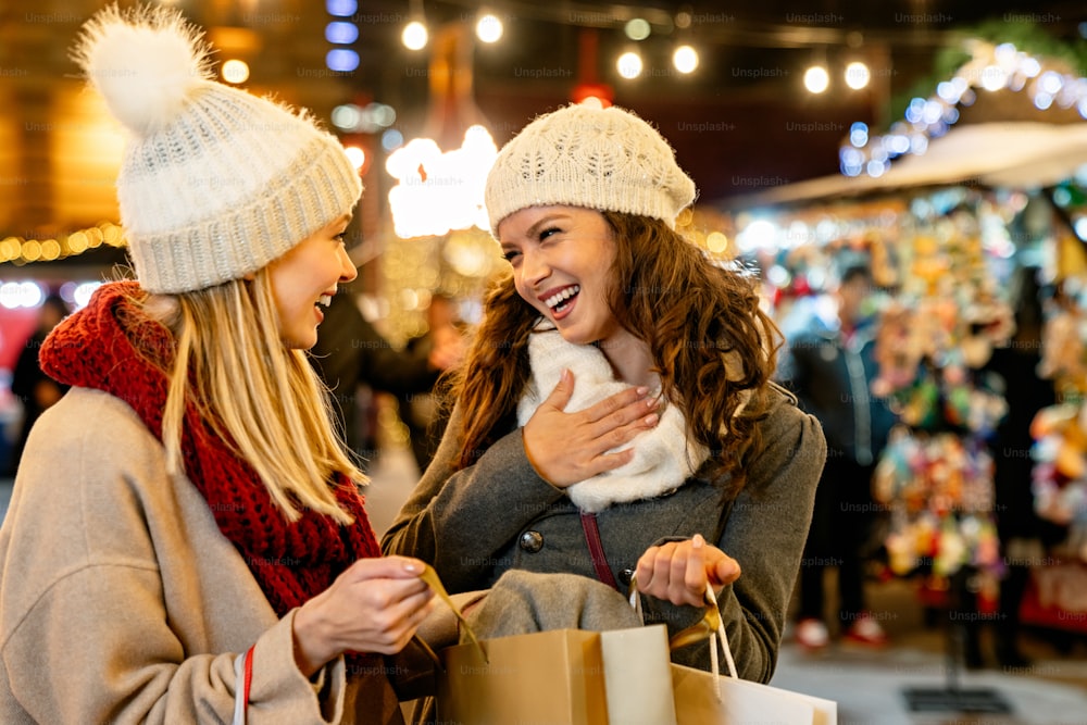 Venta de Navidad y concepto de personas. Felices amigas jóvenes con bolsas de compras disfrutando de las compras en el mercado de navidad