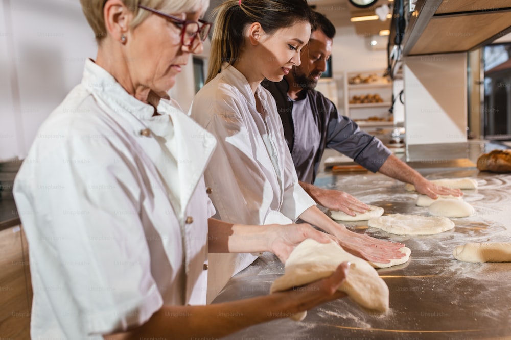 Group of bakers in uniform preparing dough for bread in modern manufacturing.
