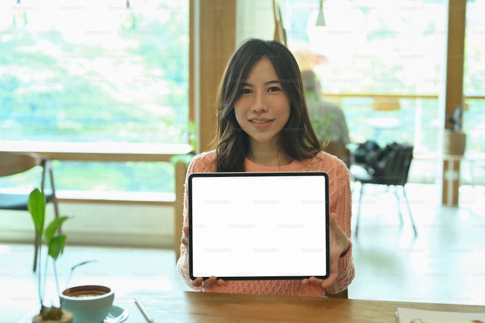 Smiling asian woman holding and showing digital tablet with empty screen.