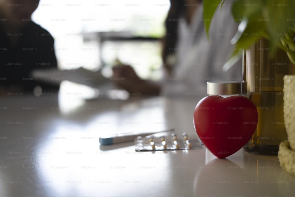 Red heart with thermometer and medical pills on white table background. Healthcare and medical concept.