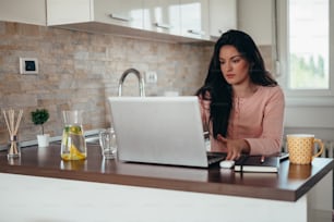 Mulher jovem bonita vestindo um pijama e usando um laptop enquanto trabalha em casa