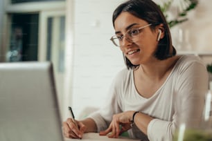 Belle femme écrivant dans un carnet et utilisant un ordinateur portable tout en gérant son entreprise et en travaillant à distance depuis chez elle