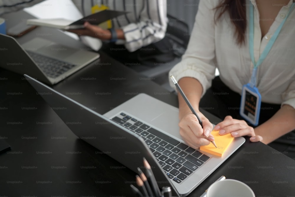 Trabajadora de oficina que trabaja con una computadora portátil y toma notas en notas adhesivas.