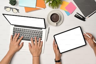 Oben sehen zwei junge Leute, die Laptop und digitales Tablet auf einem weißen Schreibtisch benutzen.