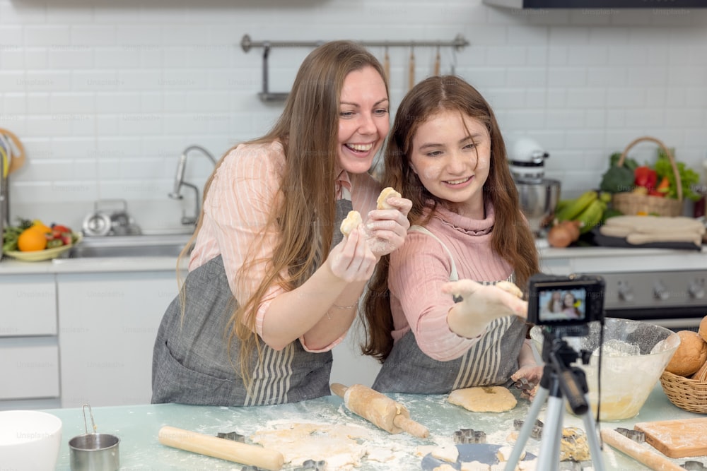 With a live digital camera in the kitchen, mother and daughter smile and have fun while preparing biscuit dough together, daughter learning how to make cookies with her mother.