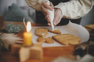 크리스마스 진저 브레드 쿠키를 촛불과 장식품으로 나무 테이블에 장식합니다. 프로스팅으로 진저 브레드 하우스 만들기를 닫습니다. 분위기 있는 분위기 있는 이미지. 휴일 준비
