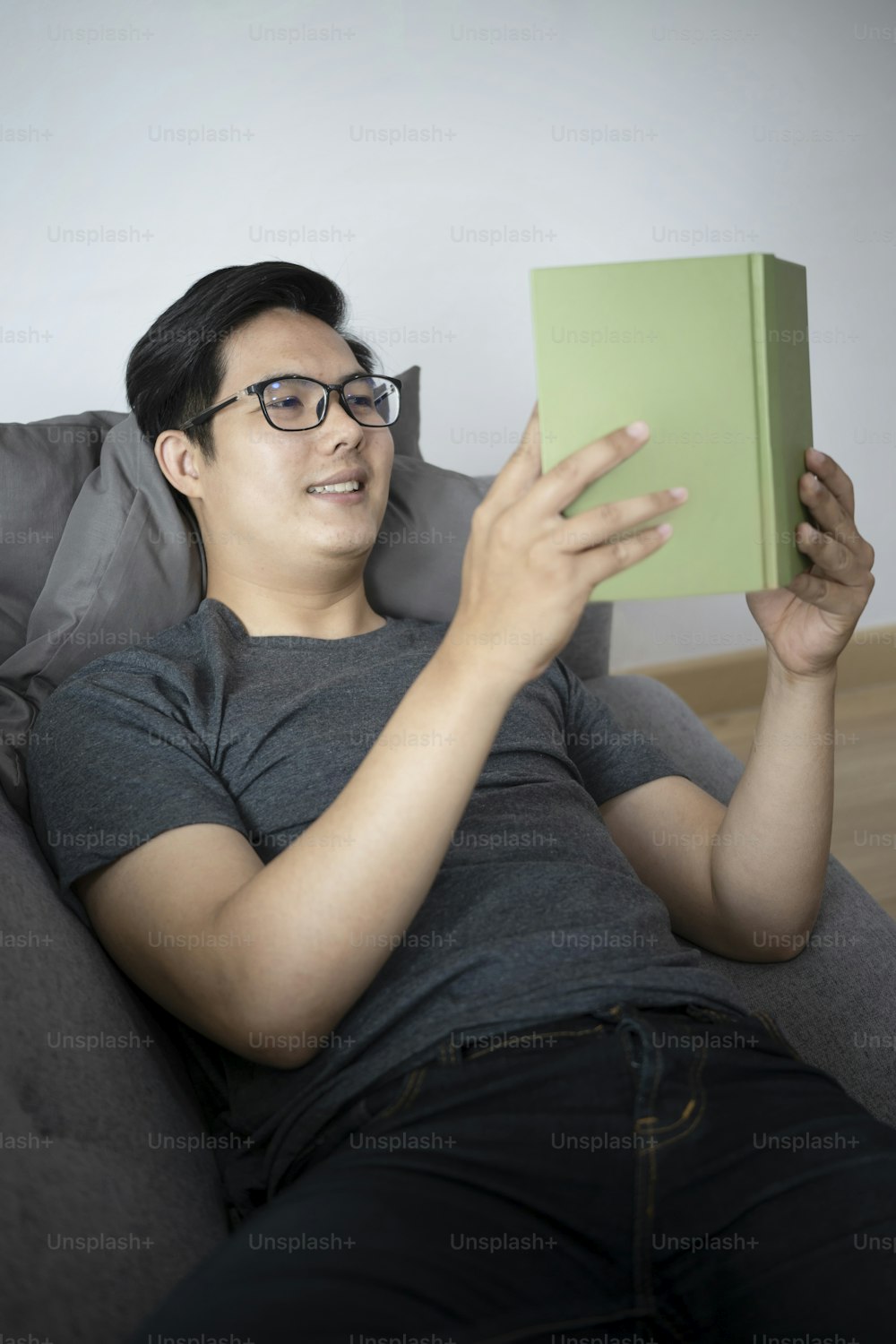 Smiling young asian man reading book on sofa.