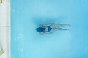 Drohnenansicht auf junge Frau, die im blauen Schwimmbad taucht