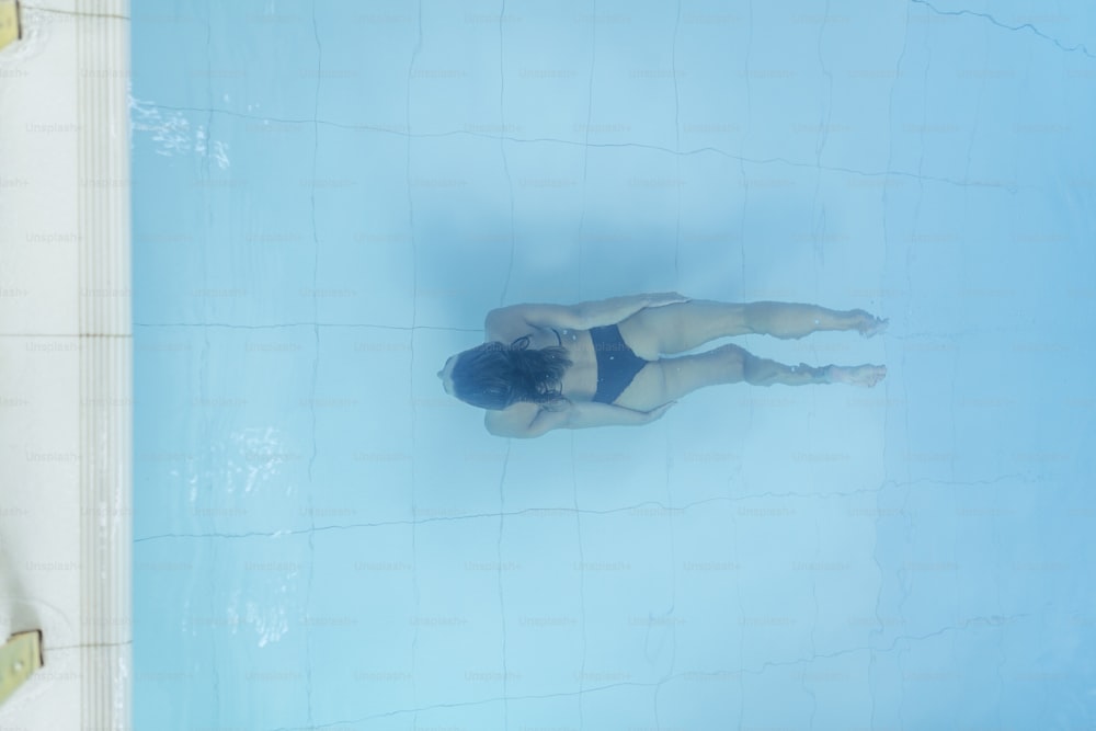 Vista del drone sulla giovane donna che si tuffa nella piscina blu