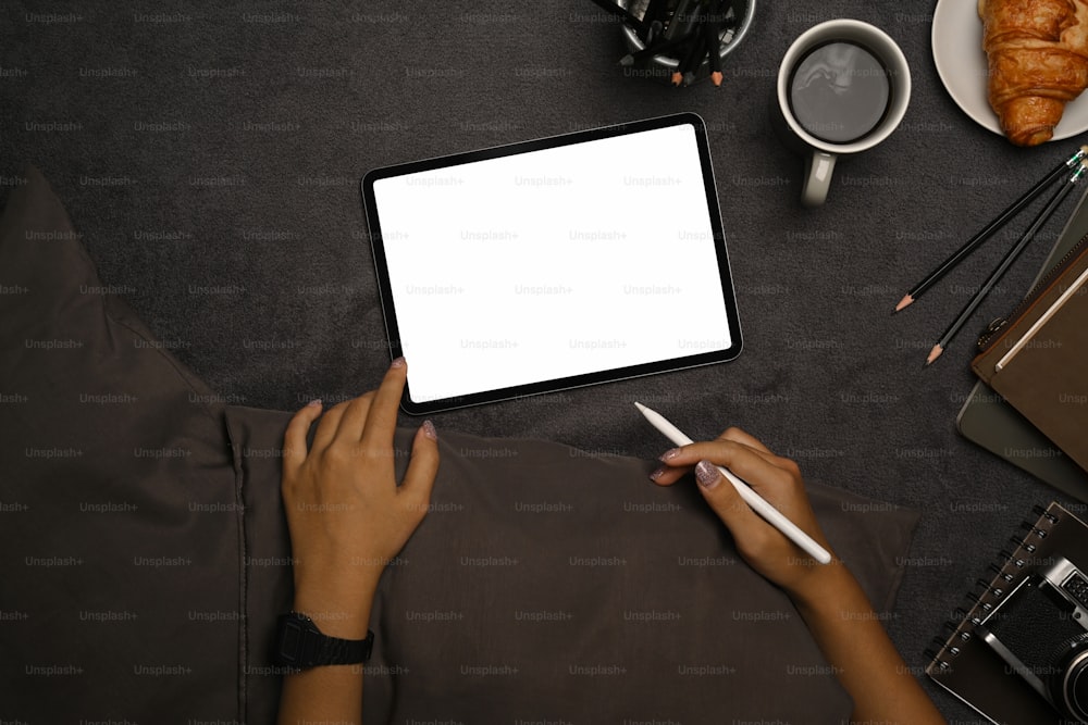 Oben sehen Sie eine junge Frau, die einen Stylus-Stift hält und ein digitales Tablet auf grauem Teppich benutzt.