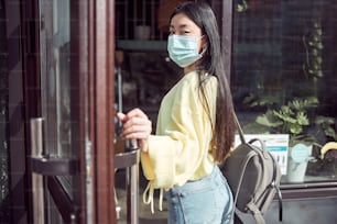 Mulher atraente e confiante em máscara de proteção segurando porta aberta enquanto entra no refeitório para pedir refeição na pandemia de covid-19