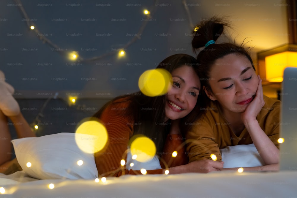 아시아 여자 친구들은 침실의 침대에 누워 노트북 컴퓨터에서 함께 영화나 온라인 쇼핑을 보고 있다. 현대 여성 커플은 집에서 함께 기술로 주말 활동 라이프 스타일을 즐긴다.